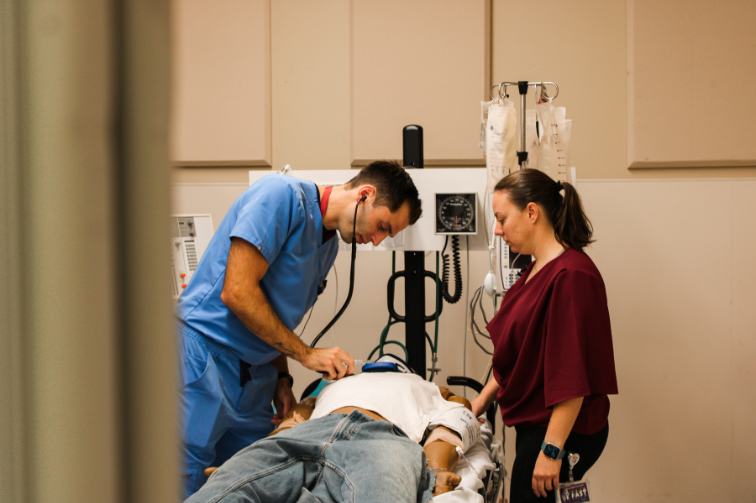 A resident listens to a mannequin's heart during a training exercise.
